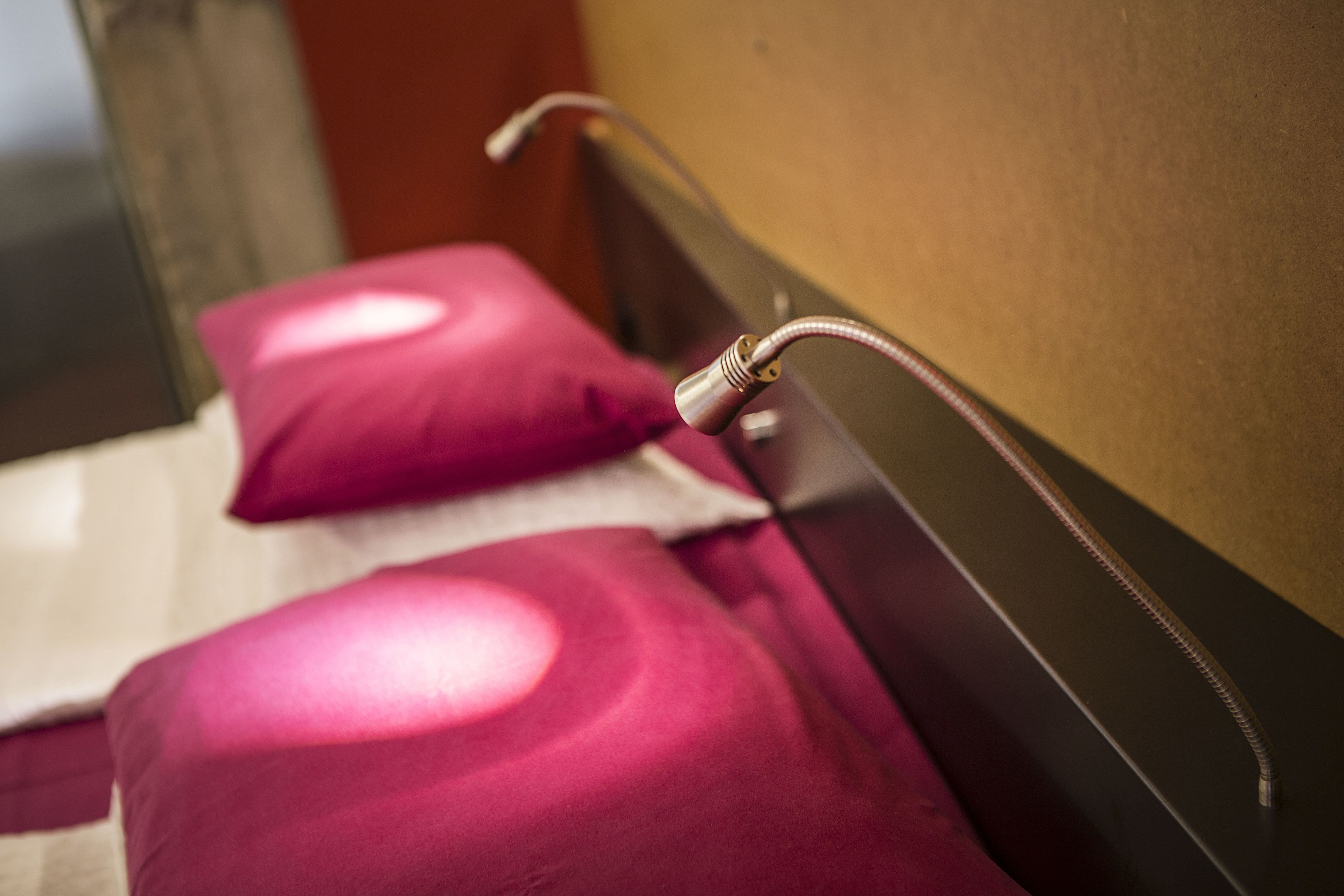 Un primo piano di un letto con testiera, un cuscino e un oggetto metallico, forse parte della struttura del letto o un dispositivo.