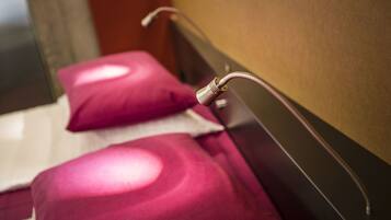 A close-up of a bed with a headboard, a pillow, and a metallic object, possibly a part of the bed frame or a device.