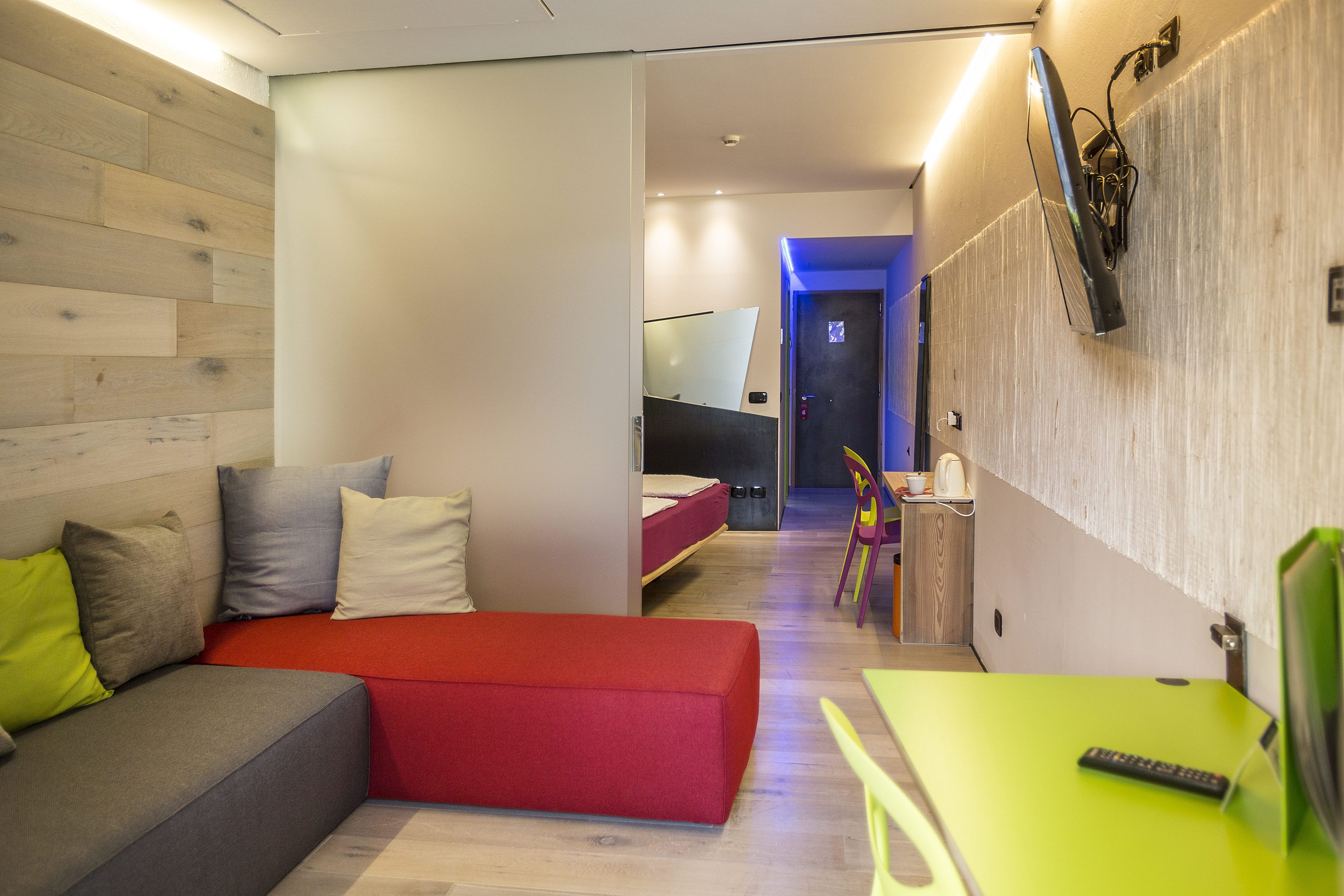 Una habitación de hotel moderna con un sofá rojo, una mesa verde y una cama con colchón rojo.