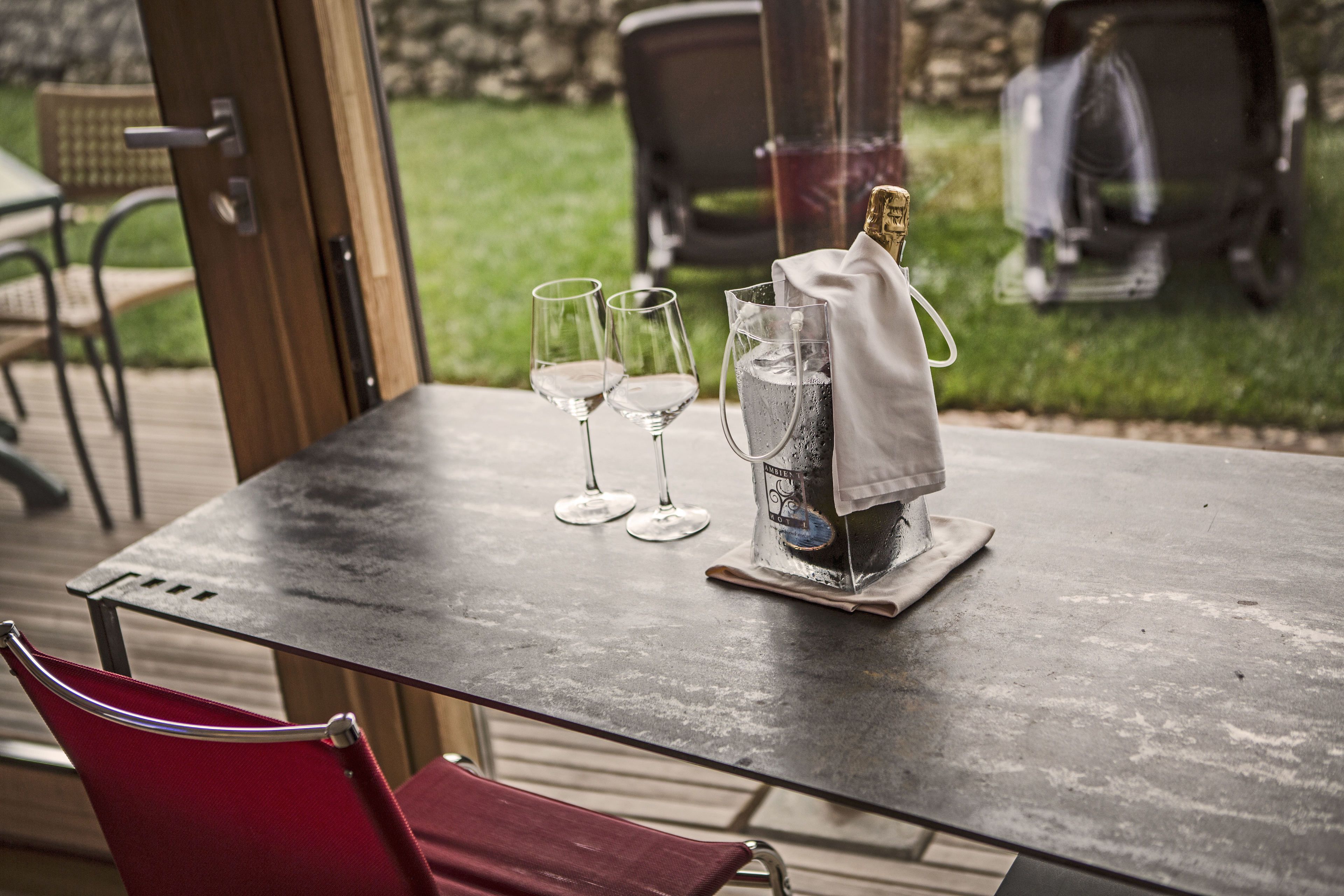 Una mesa con dos copas de vino, una botella de champán y una jarra de agua en un patio.
