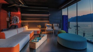 A modern living room with a sofa, chairs, a coffee table, and a view of the water. - Ambienthotel Primaluna (Malcesine)