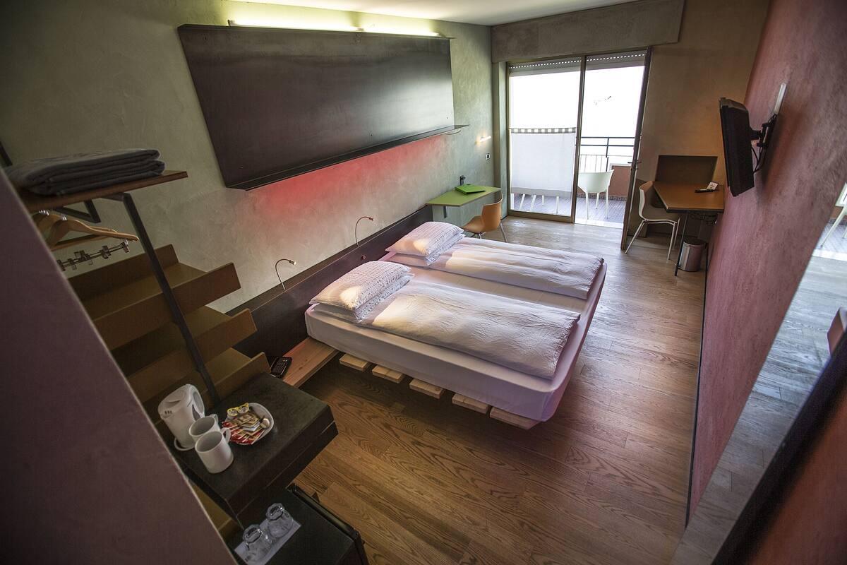 A room with two beds, a desk, a chair, and a TV mounted on the wall.
