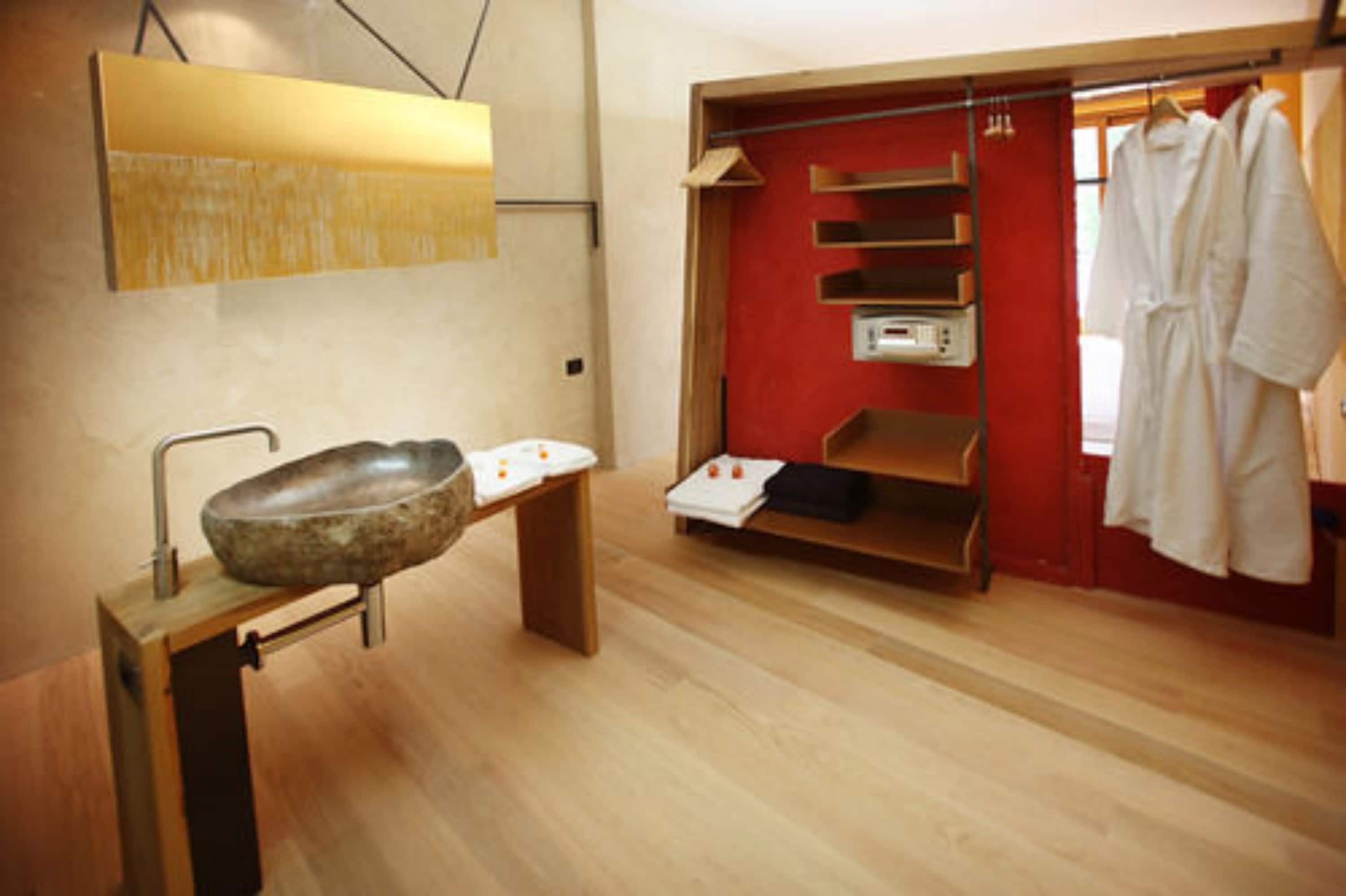 A modern bathroom with a large stone sink, wooden shelves, and a red wall.