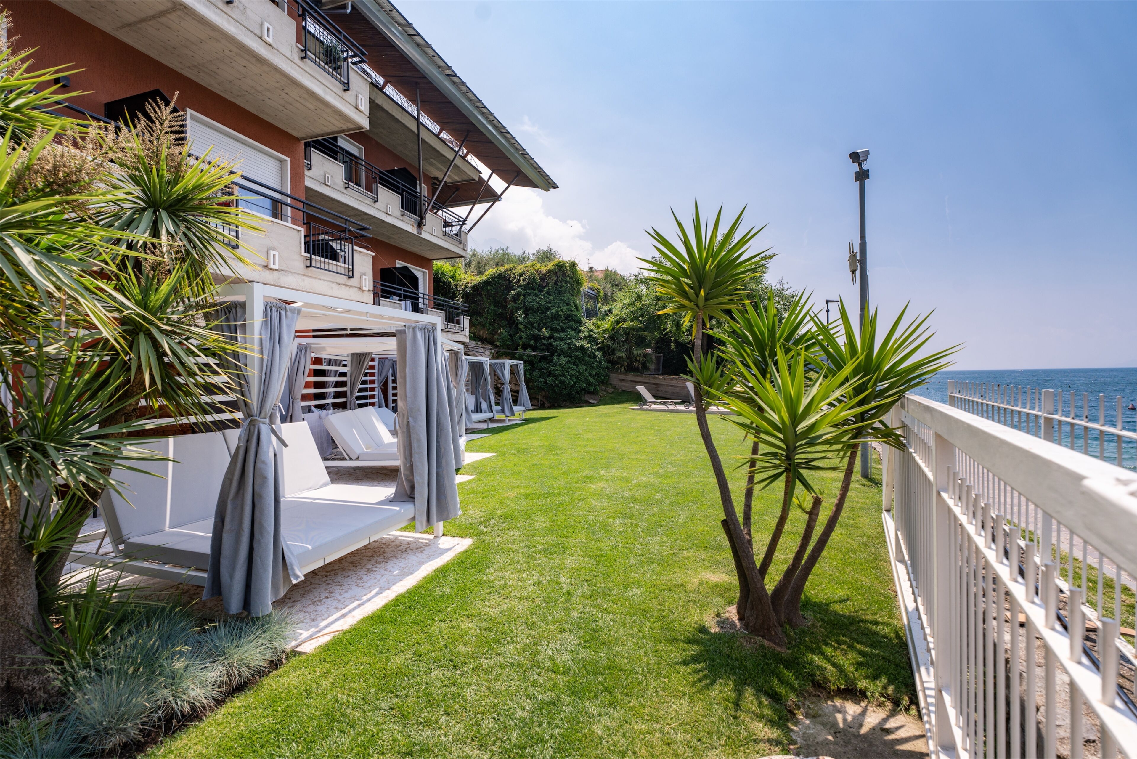A balcony with a view of the sea, a grassy lawn, and a white fence.