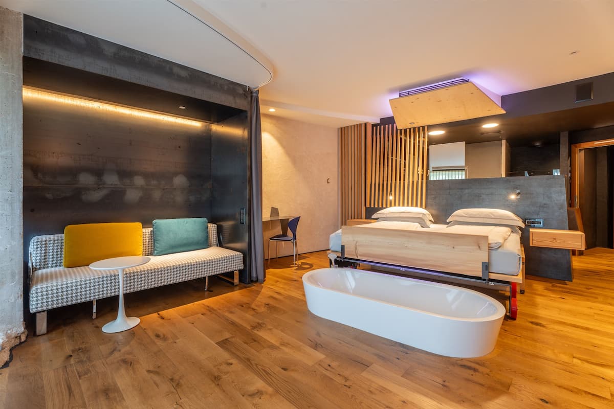 A modern bedroom with a large bed, a built-in bathtub, and a sofa with cushions.
