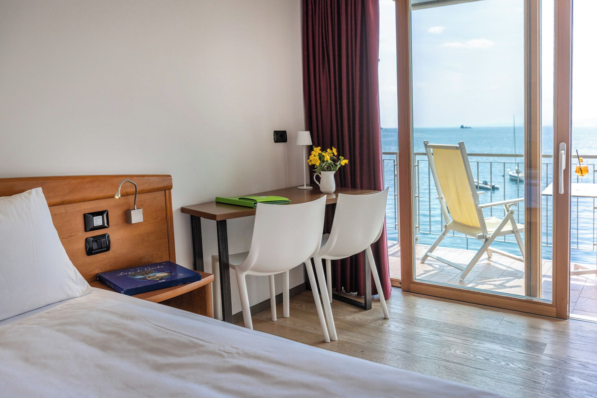 Ein Hotelzimmer mit Bett, Schreibtisch mit Stühlen, Meerblick und einem Balkon mit einem Sessel.