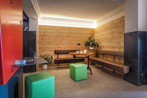 Un interior moderno con paneles de madera, un banco de madera, un reposapiés verde, una mesa con una planta y un mueble de madera en rojo y azul.