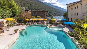 Piscina con tumbonas y sombrillas, rodeada de edificios y un paisaje montañoso.