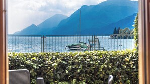 Vista de un lago con barcos, montañas y un seto al frente.