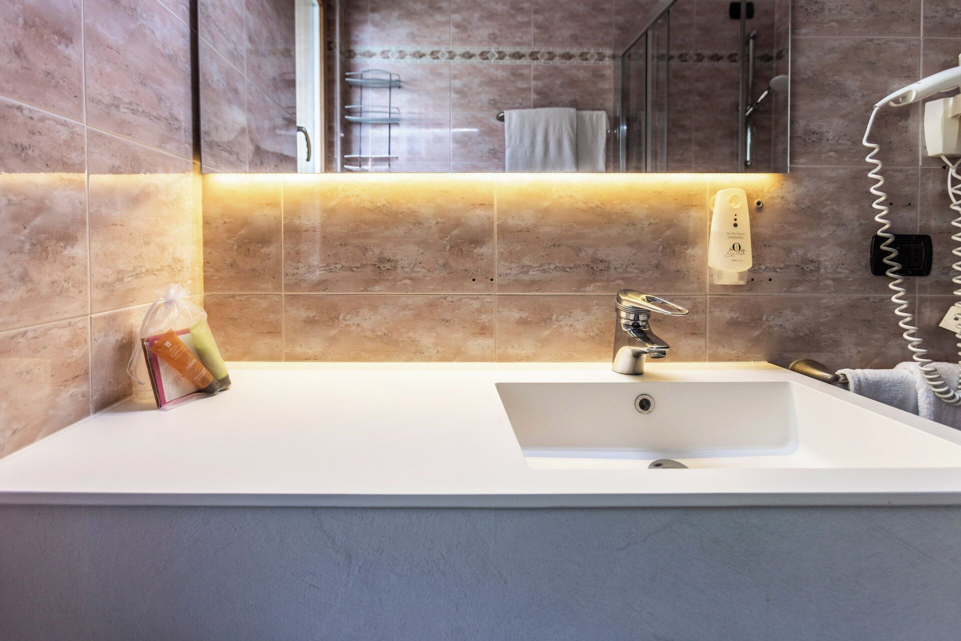 Ein modernes Badezimmer mit einem weißen Waschbecken, einer Handbrause, einem Handtuchhalter und einem Spiegel.