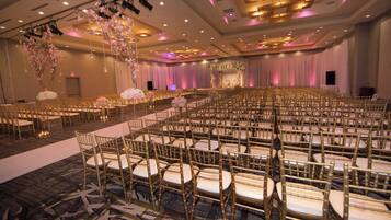 A banquet hall with rows of gold chairs and tables, a stage with floral decorations, and a carpeted floor.