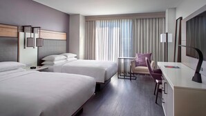 A hotel room with two beds, a desk, a chair, and a large window with curtains.