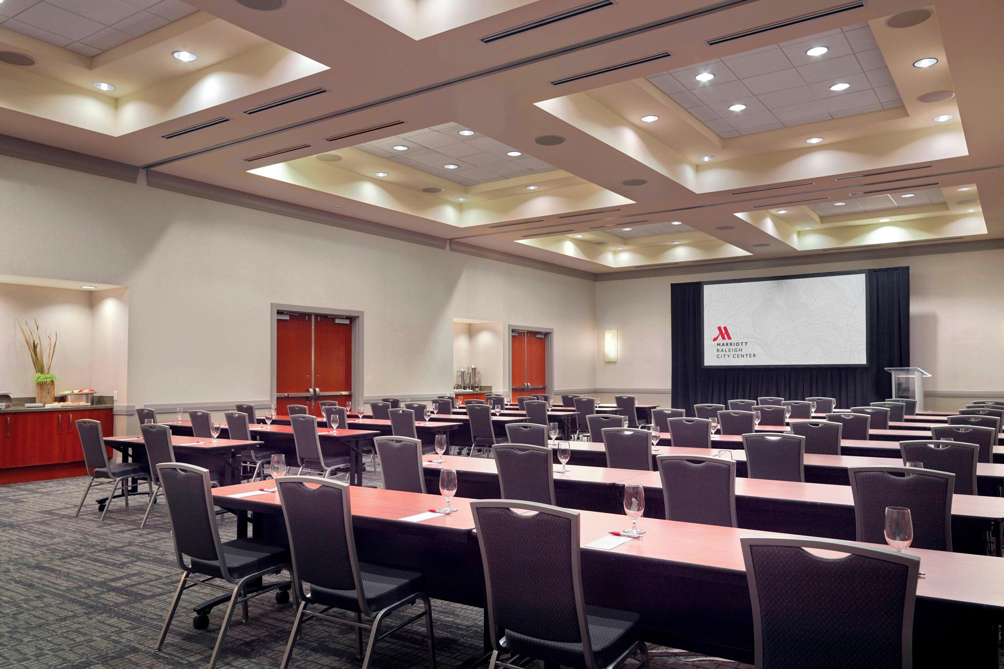 A conference room with multiple tables and chairs, a podium, and a screen displaying the Marriott logo.