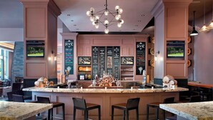 A bar area with a central island, multiple seating options, and a menu board displaying various drink options. - Raleigh Marriott City Center (Raleigh)
