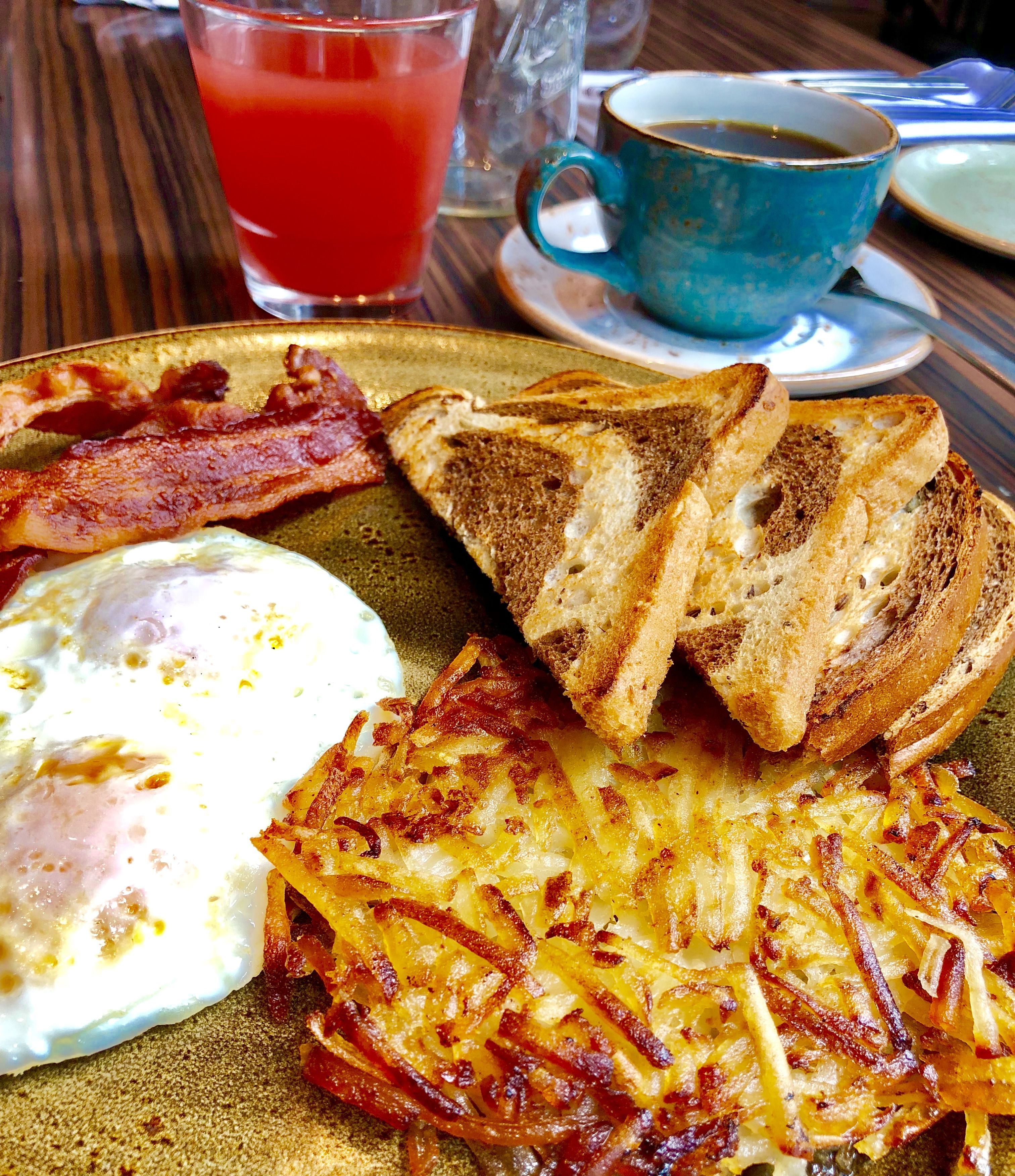A breakfast plate with toast, bacon, an egg, and hash browns.