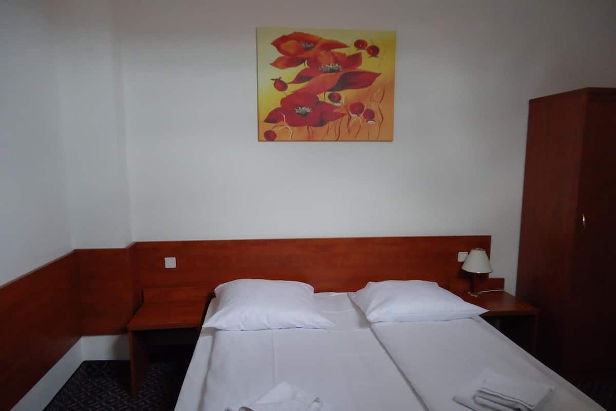 Une chambre d’hôtel avec deux lits simples, une tête de lit en bois, une table de chevet avec une lampe et un tableau au mur.