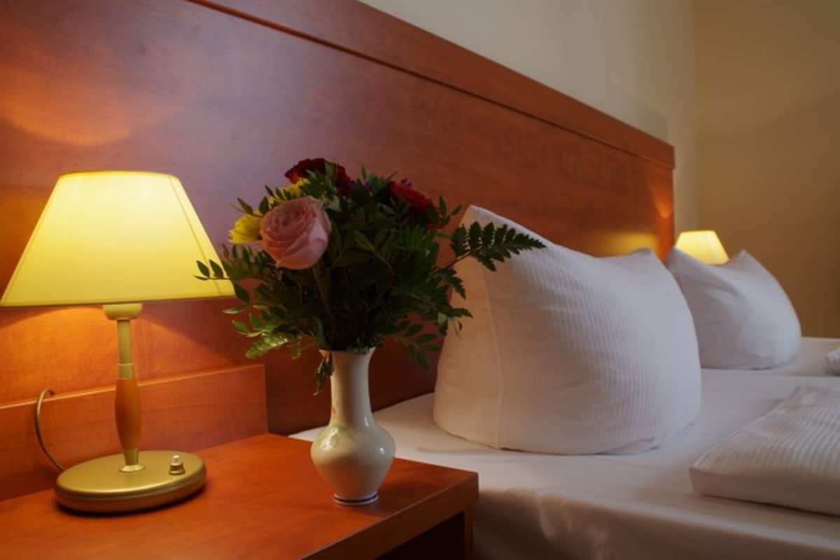 Une chambre d’hôtel avec une tête de lit en bois, une table de chevet avec une lampe et un vase de fleurs.