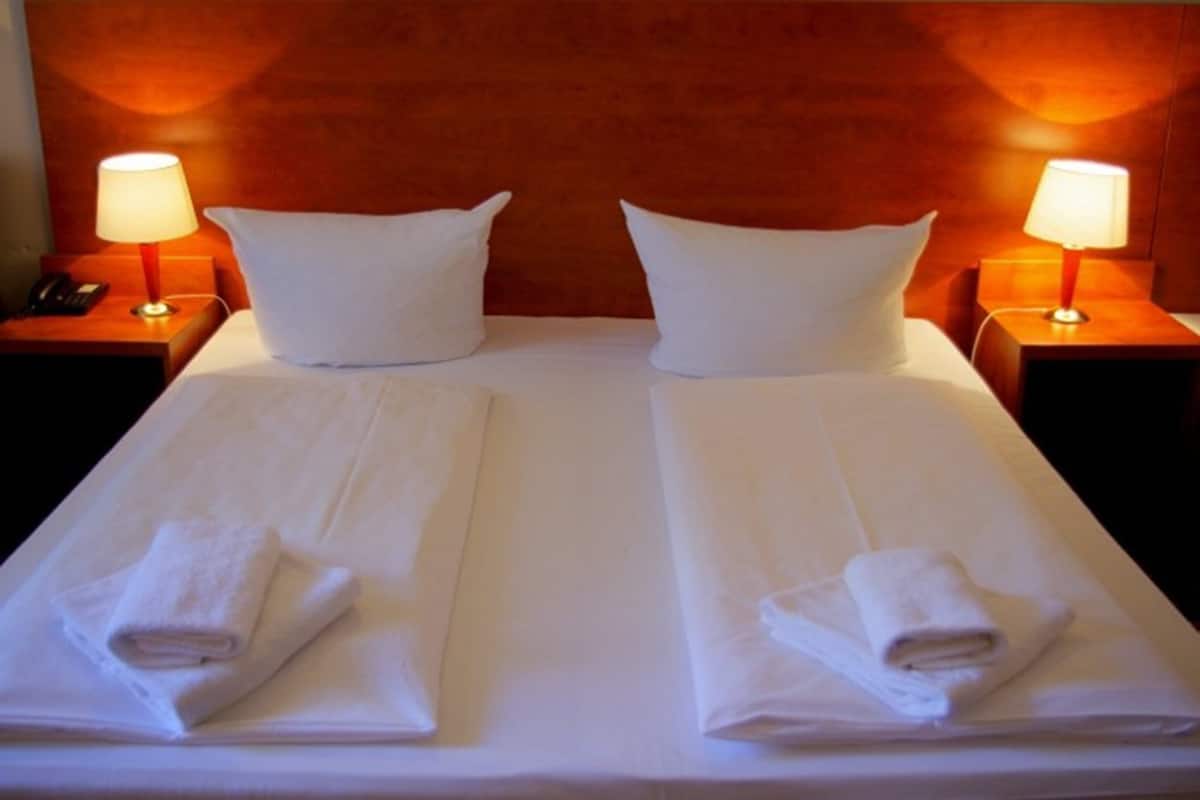 Un lit double avec du linge de lit blanc et deux oreillers, de chaque côté duquel se trouvent des tables de chevet avec des lampes, dans une pièce aux murs lambrissés.