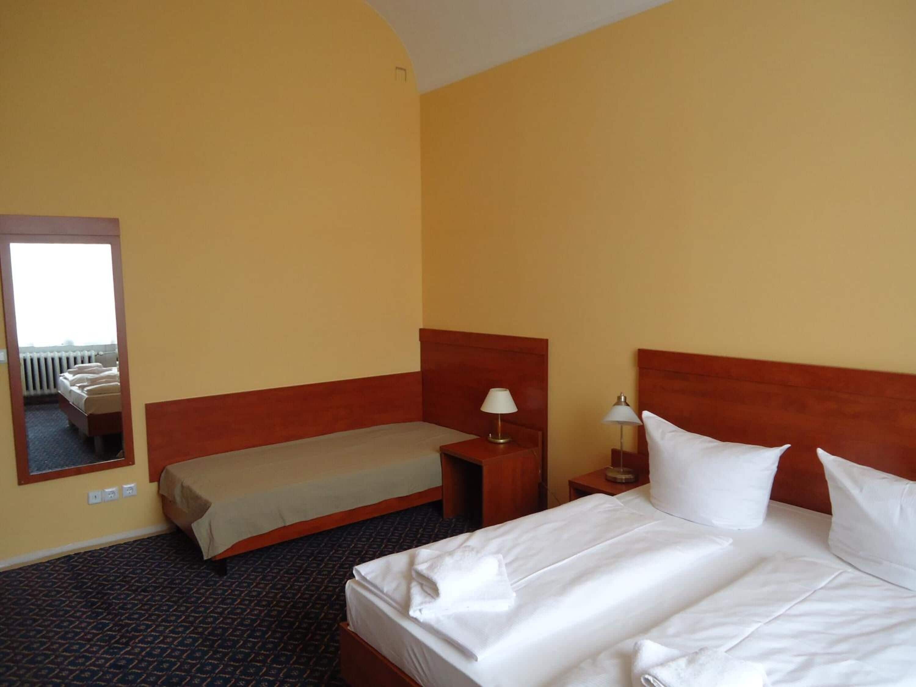 Ein Hotelzimmer mit einem großen Bett, einem Einzelbett, einem Nachttisch mit Lampen und einem Spiegel an der Wand.