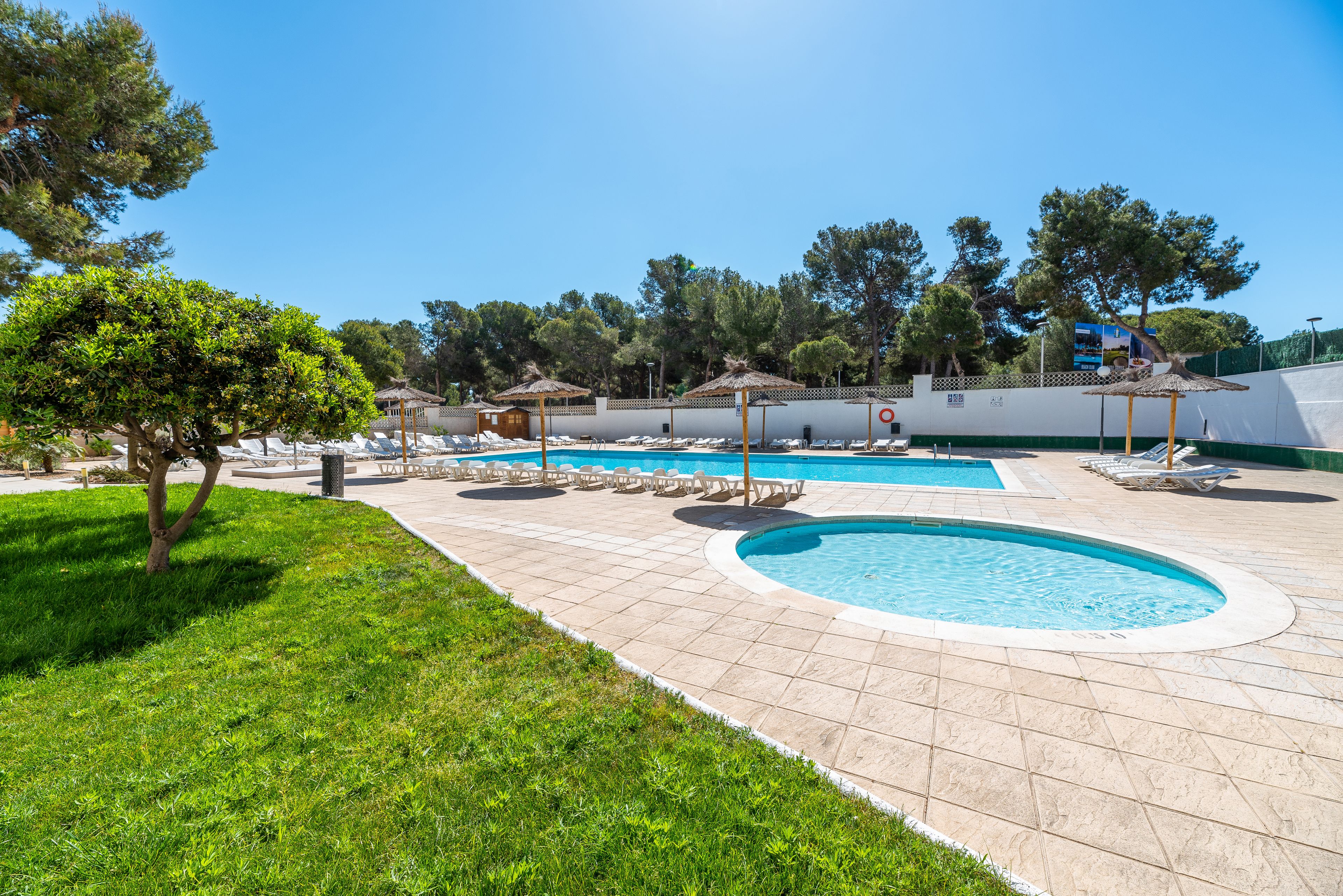 A pool area with two pools, lounge chairs, and umbrellas.