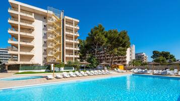 A swimming pool with lounge chairs and umbrellas, surrounded by a multi-story building with balconies.