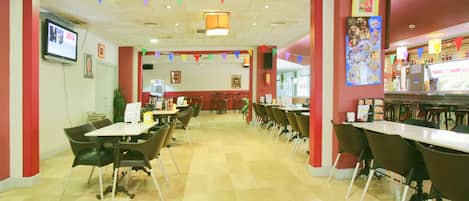 A restaurant with multiple tables and chairs, a television mounted on the wall, and colorful triangular flags hanging from the ceiling.