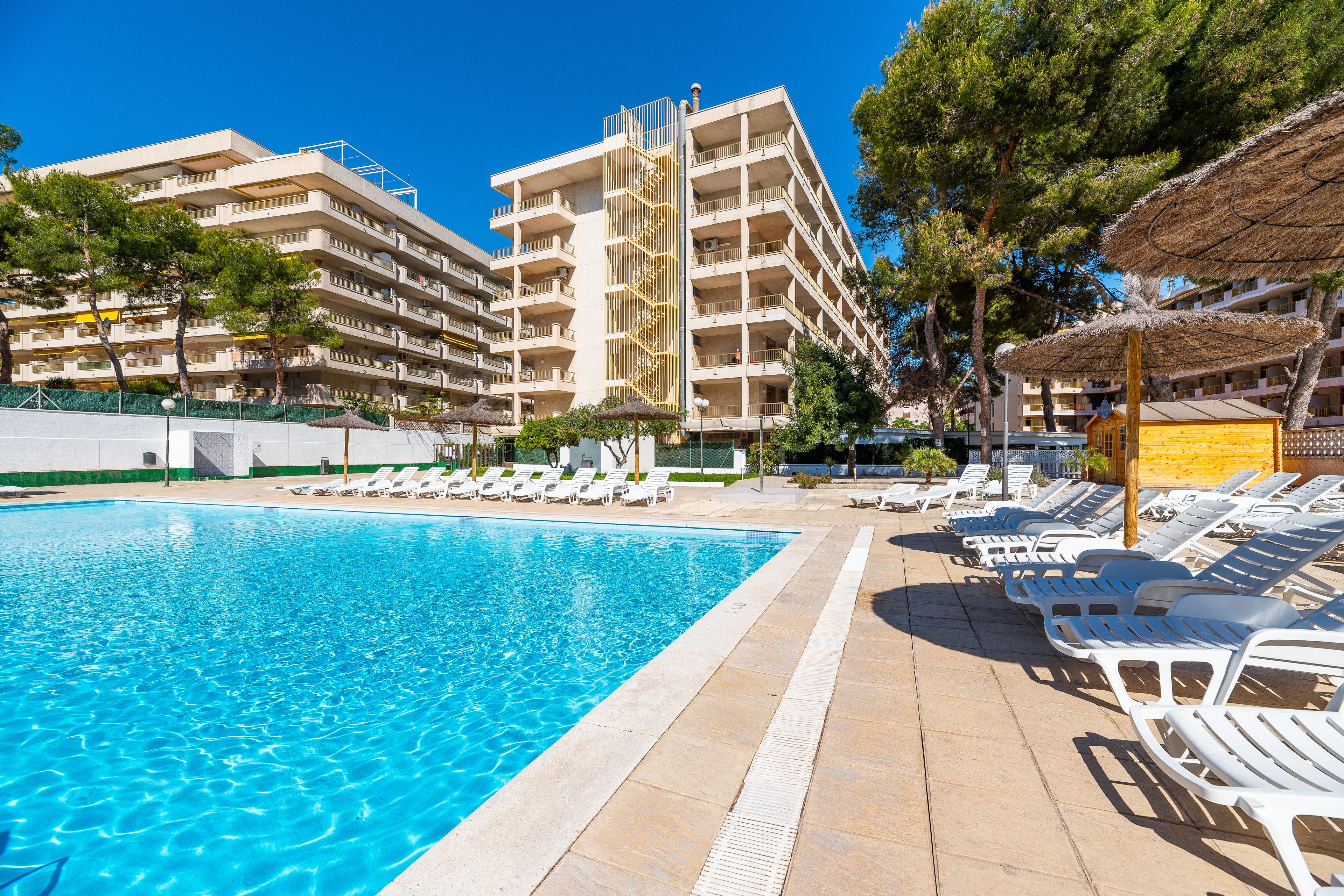A swimming pool with lounge chairs and a multi-story building in the background.