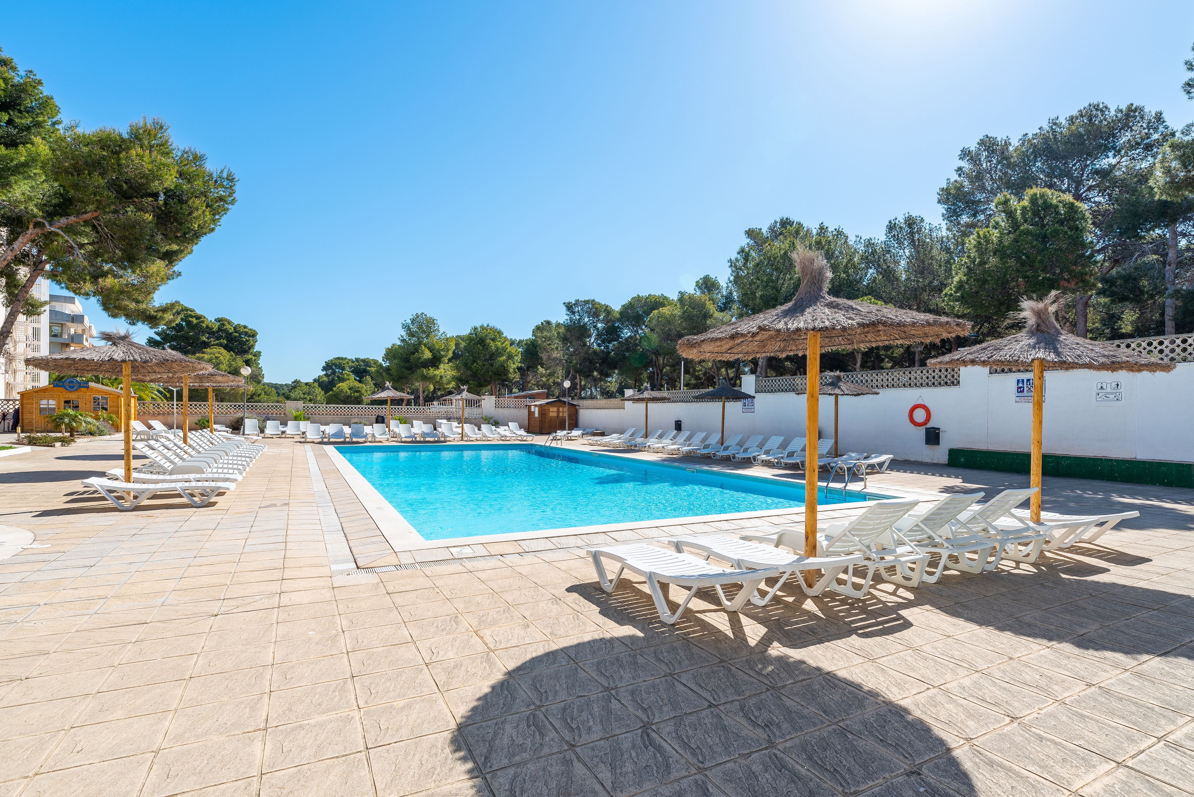 Una piscina con sillas de descanso y sombrillas, rodeada de árboles y edificios.