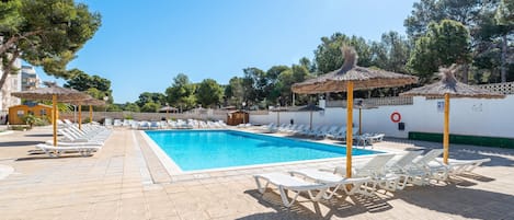 Una piscina con sillas de descanso y sombrillas, rodeada de árboles y edificios.