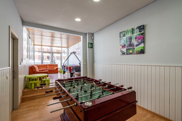 Una habitación con mesa de futbolín, un sofá y una mesa con sillas.