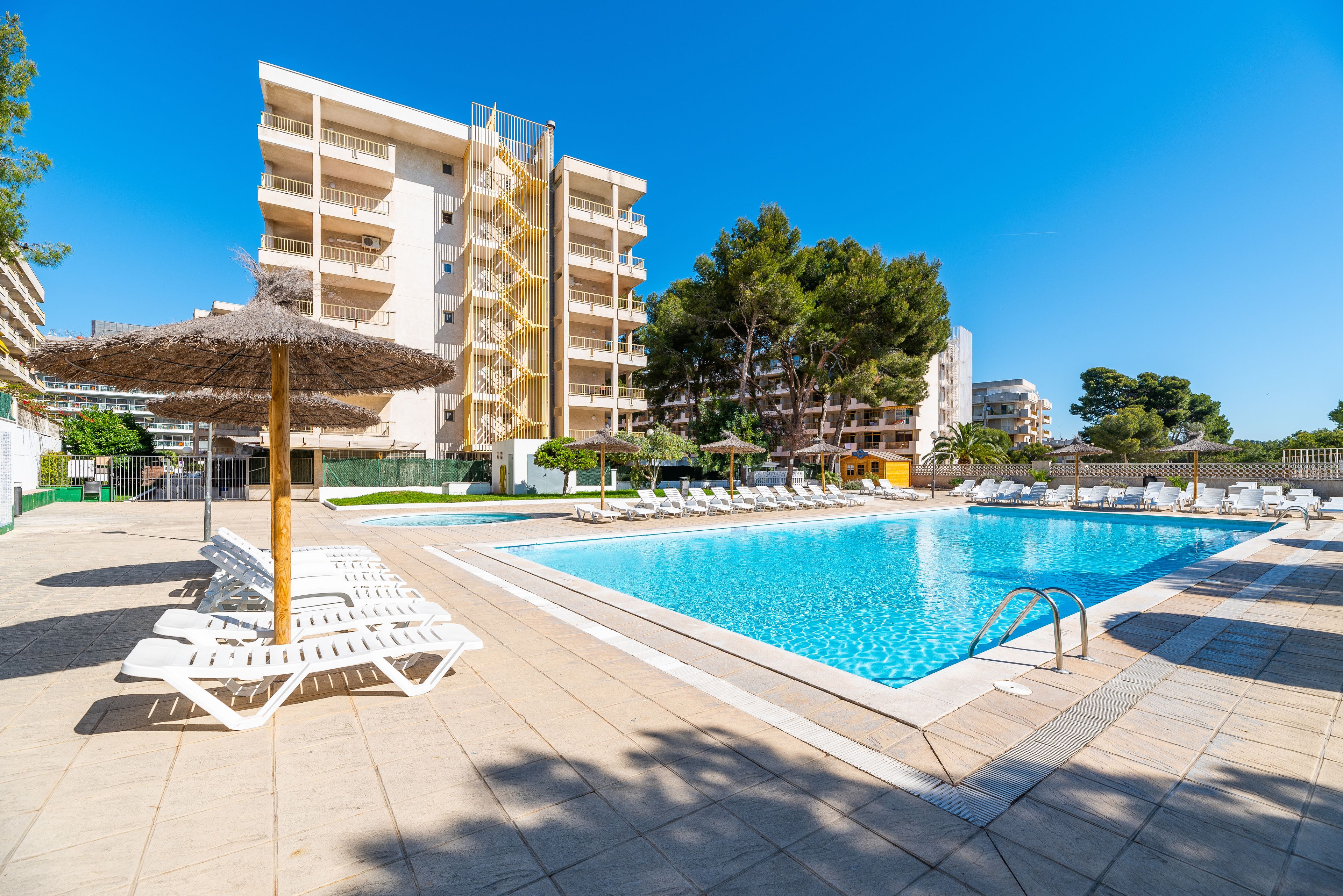 A swimming pool with lounge chairs and umbrellas, surrounded by buildings and trees.