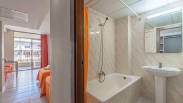 Habitación de hotel con baño que incluye una bañera, un lavamanos y una ducha.