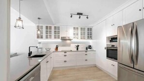 A modern kitchen with white cabinetry, stainless steel appliances, and a wooden floor.