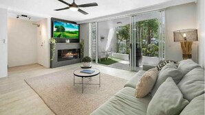 A modern living room with a fireplace, a ceiling fan, a large TV, and a balcony with glass doors.