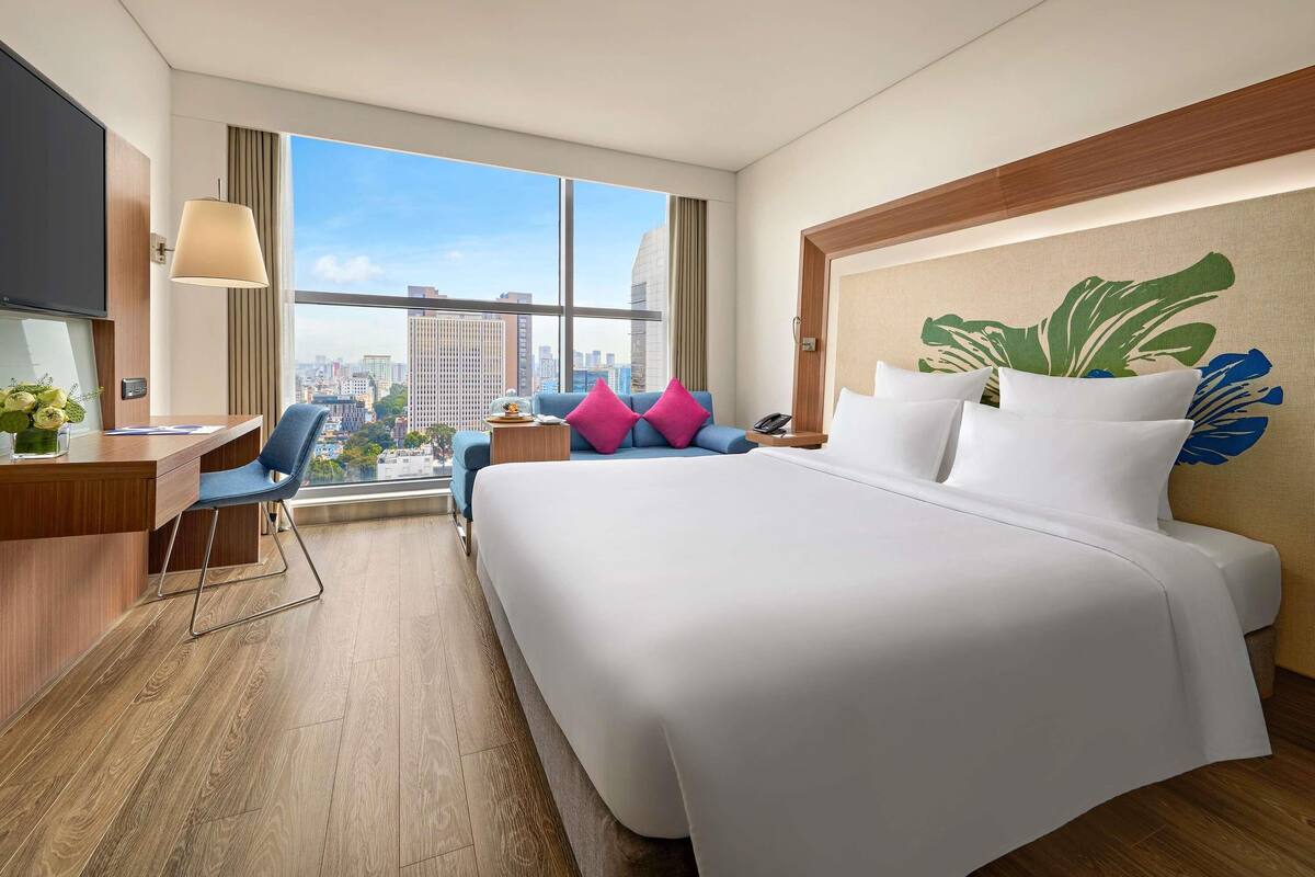Een hotelkamer met een groot bed, een bureau, een stoel en uitzicht op de stad.