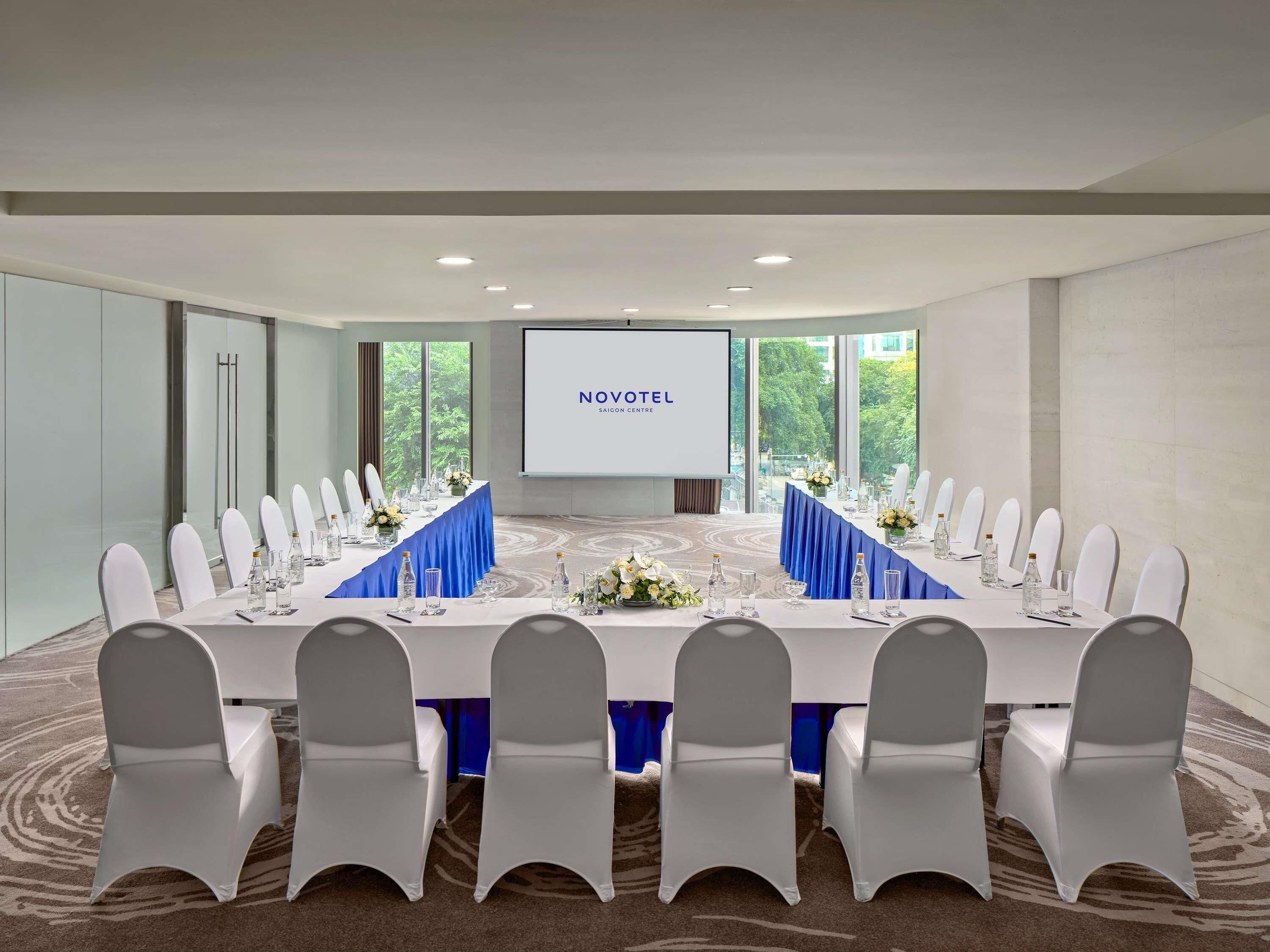 A conference room with a long table, white chairs, and a screen displaying 'NOVOTEL SAIGON CENTRE'.