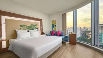 A modern hotel room with a large bed, a blue armchair, and a city view.