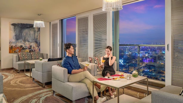 A modern hotel room with a city view, a large painting on the wall, and a dining area with a table and chairs.