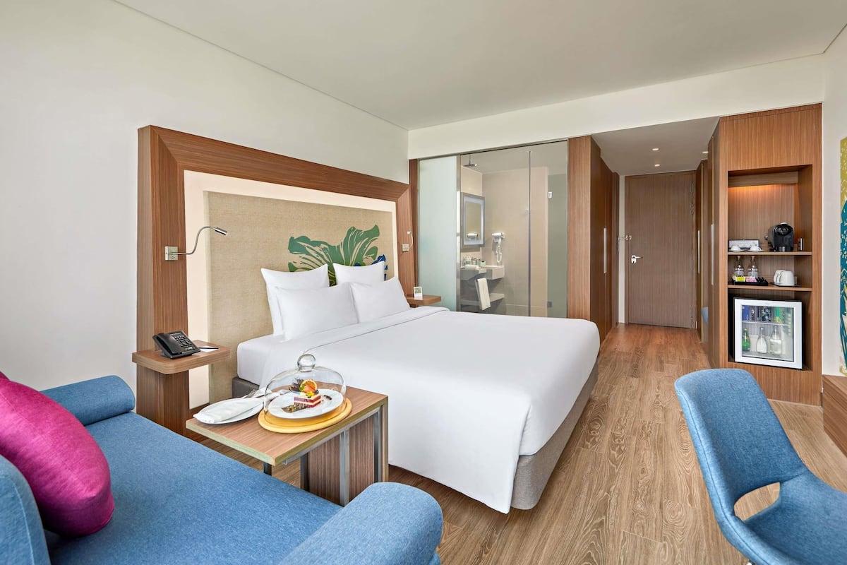 Hotelkamer met een bed, een bureau met telefoon, een stoel, een klein tafeltje met eten erop, en een douchecabine met glazen wanden.