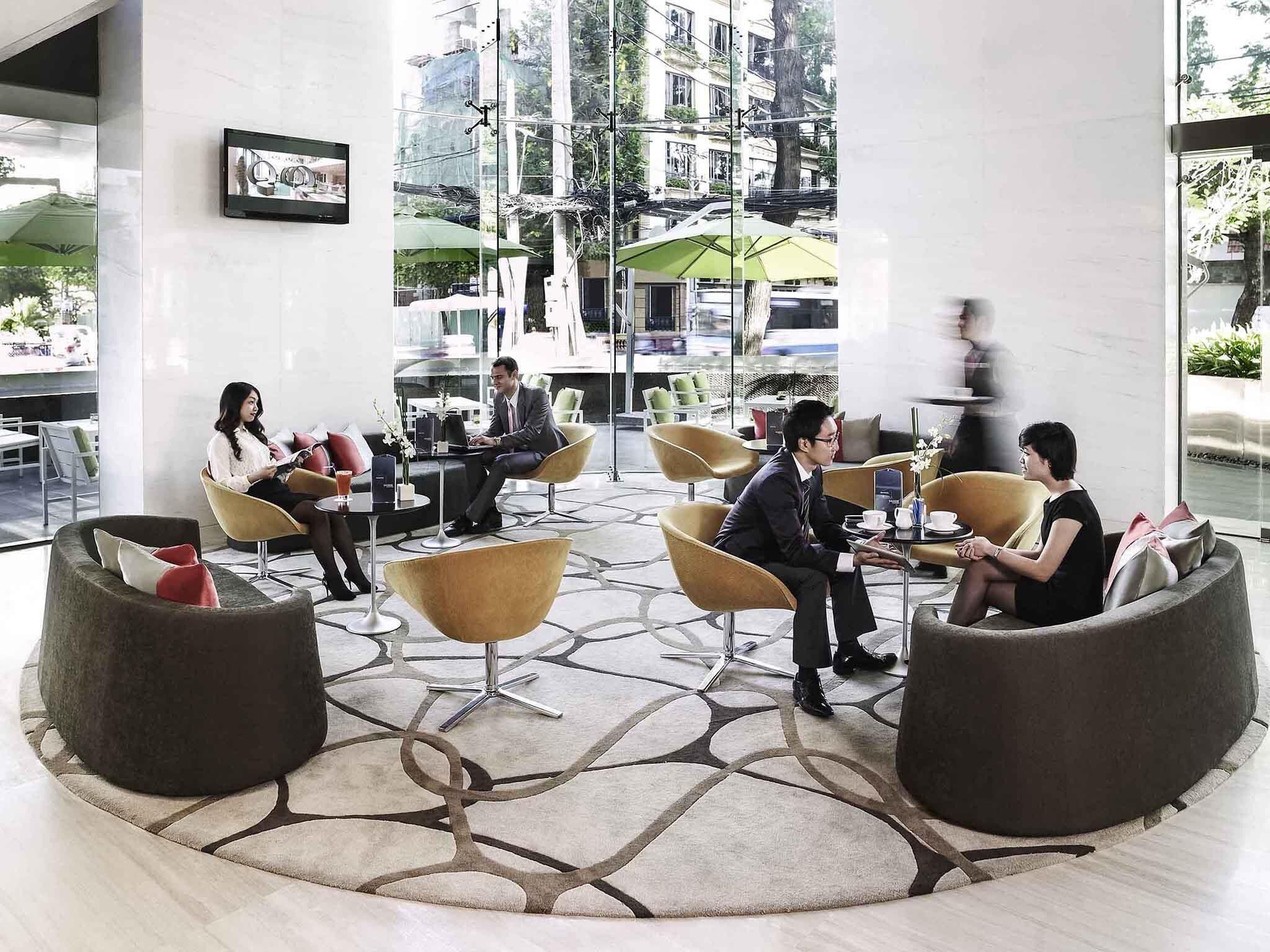 Un área de estar moderna en el interior, con sillas redondas y un suelo estampado, ventanas amplias y vistas al exterior.