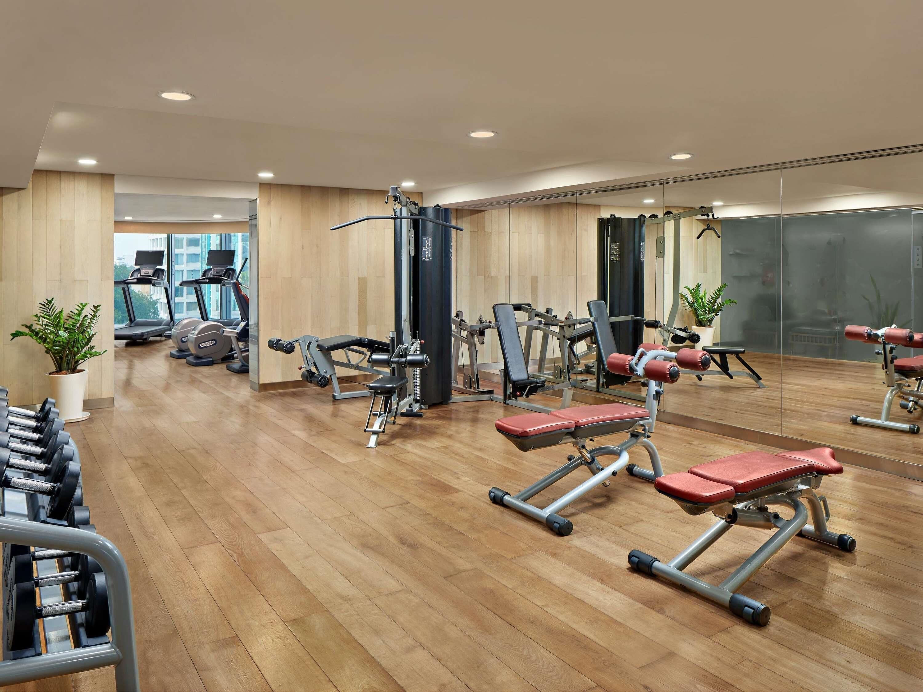 Ein Fitnessraum mit Trainingsgeräten, Holzboden und großen Fenstern.