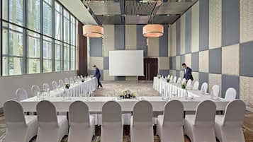 A conference room with long tables, white chairs, and a large screen.