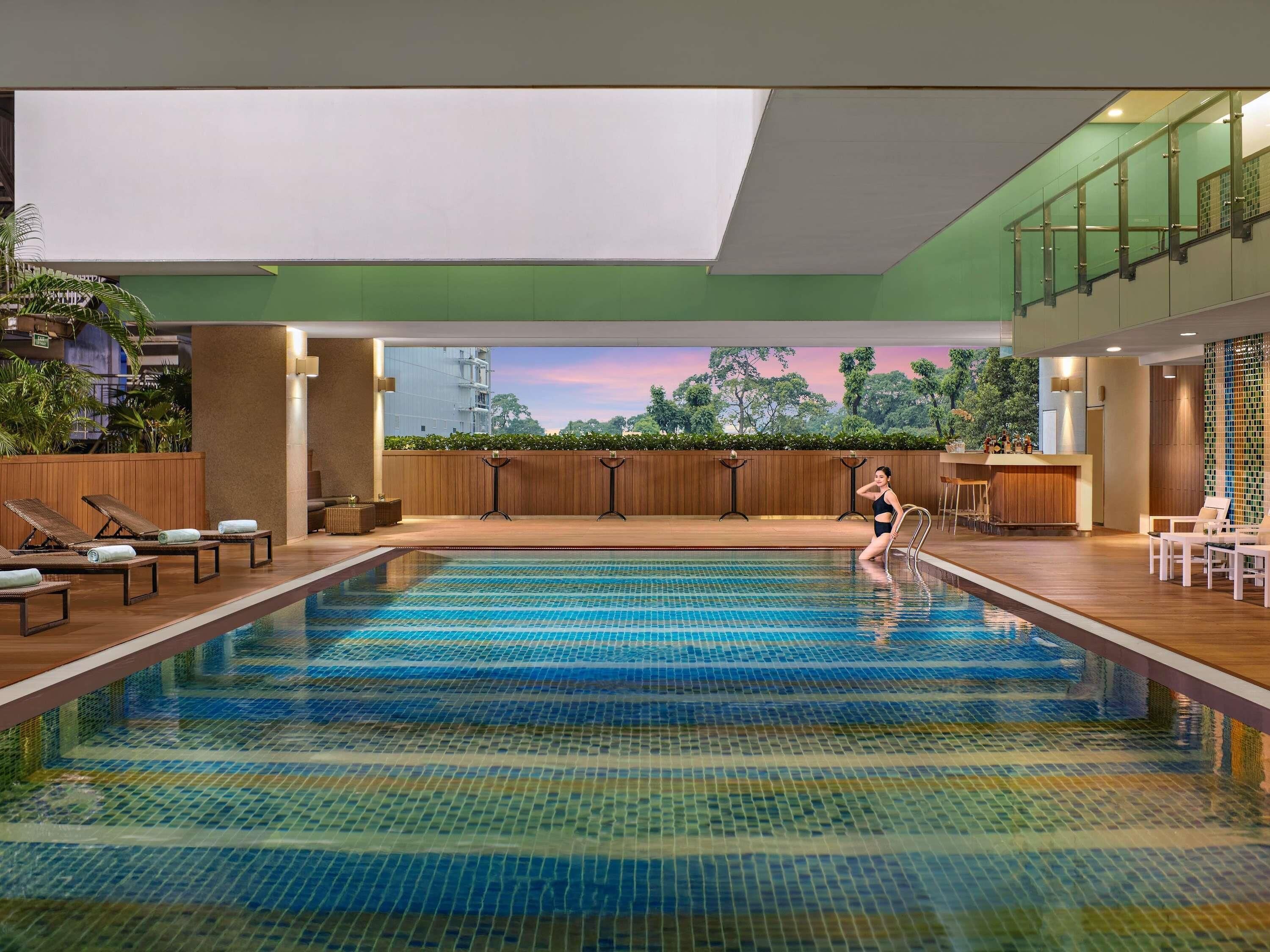Piscina interior com vista para árvores e um edifício através do muro de vidro.