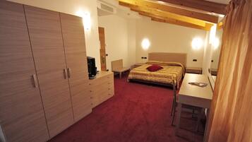 A bedroom with a large wardrobe, a bed with a red pillow, a bedside table, and a desk with a chair.