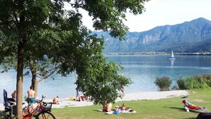 A lakeside setting with people relaxing on the grass, a sailboat on the water, and mountains in the background. - Nature Bio Hotel Elite (Levico Terme)