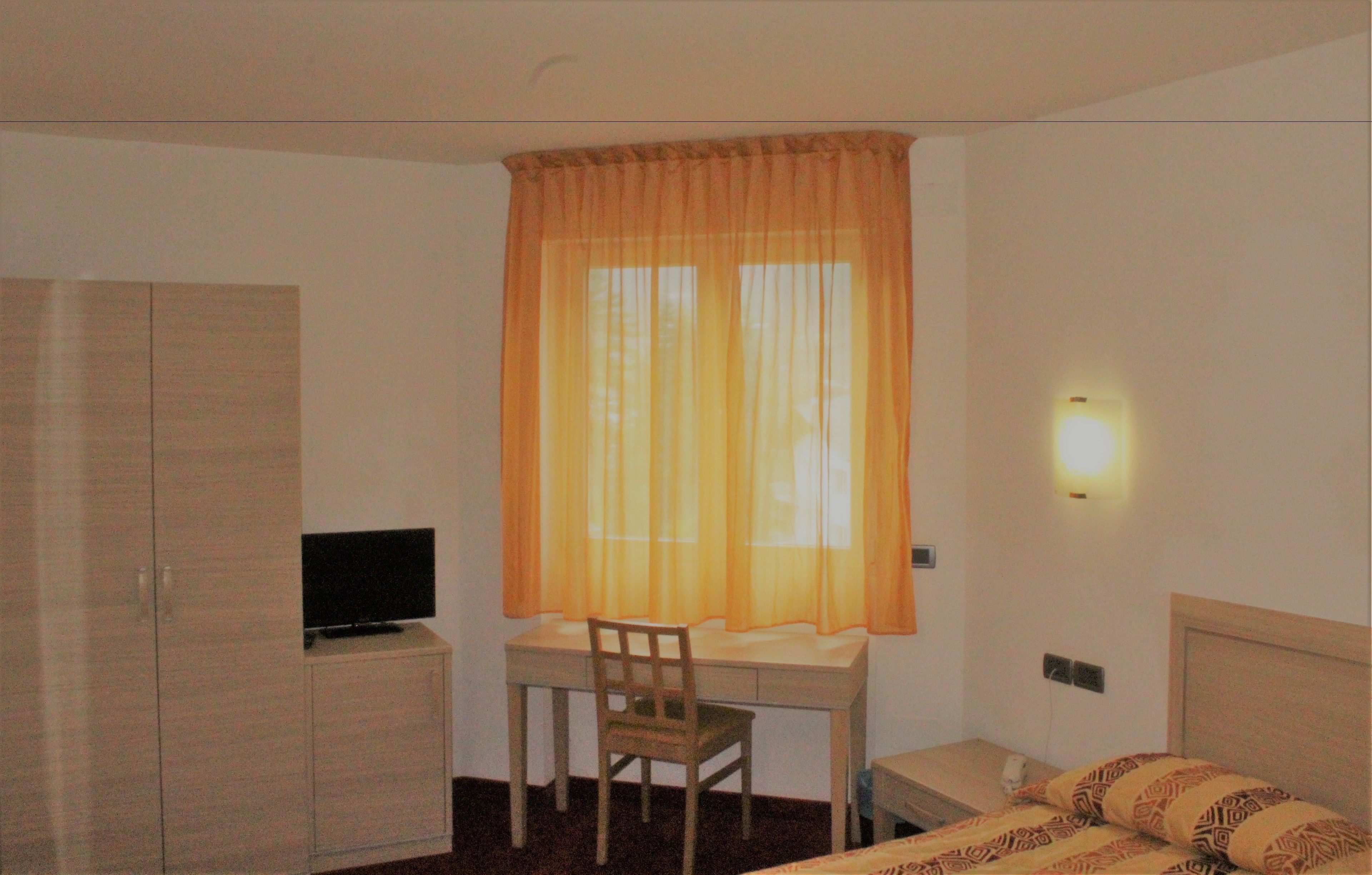 A hotel room with a desk, chair, bed, and wardrobe.