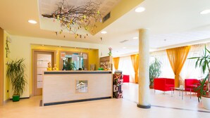 A hotel lobby with a reception desk, red seating area, and potted plants. - Nature Bio Hotel Elite (Levico Terme)