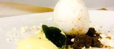 A dessert with a scoop of ice cream, a dollop of sauce, and a mint leaf on a white plate.