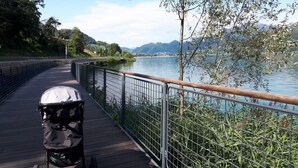 A wooden boardwalk with a stroller, overlooking a calm lake with mountains in the background. - Nature Bio Hotel Elite (Levico Terme)