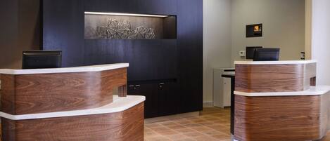 A reception area with two wooden reception desks, a dark wall with a geometric light fixture, and a tiled floor.